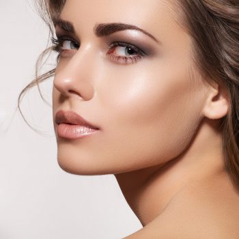 Glamour portrait of beautiful woman model with fresh daily makeup and romantic wavy hairstyle. Fashion shiny highlighter on skin, sexy gloss lips make-up and dark eyebrows